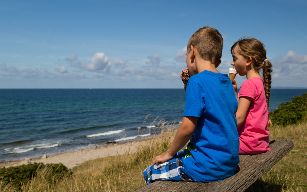 Two children travelling on holidays sitting on a bench at the beach eating ice-cream overlooking the ocean